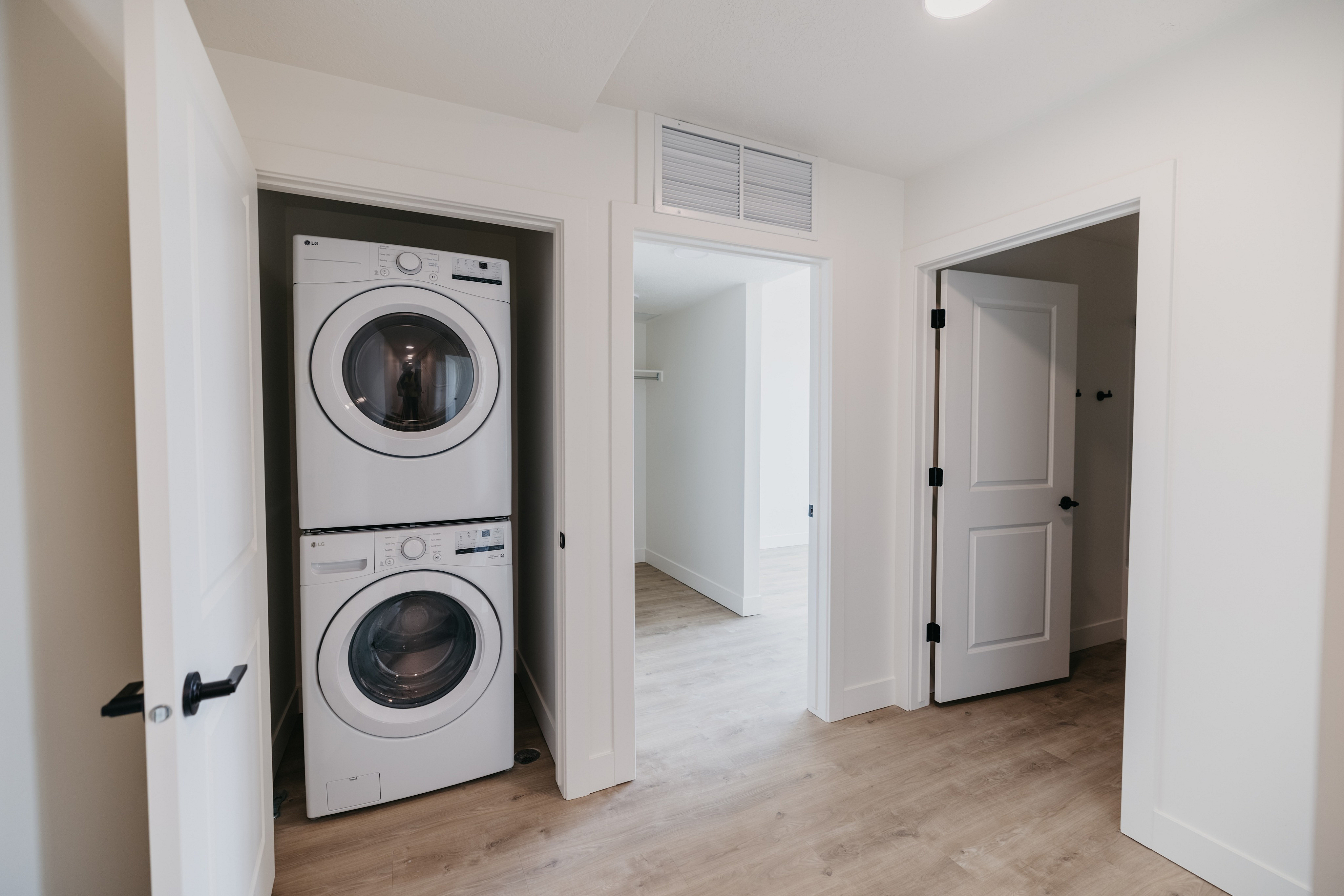 Modern laundry nook with stacked washer and dryer, adjacent to spacious rooms with sleek wooden flooring.