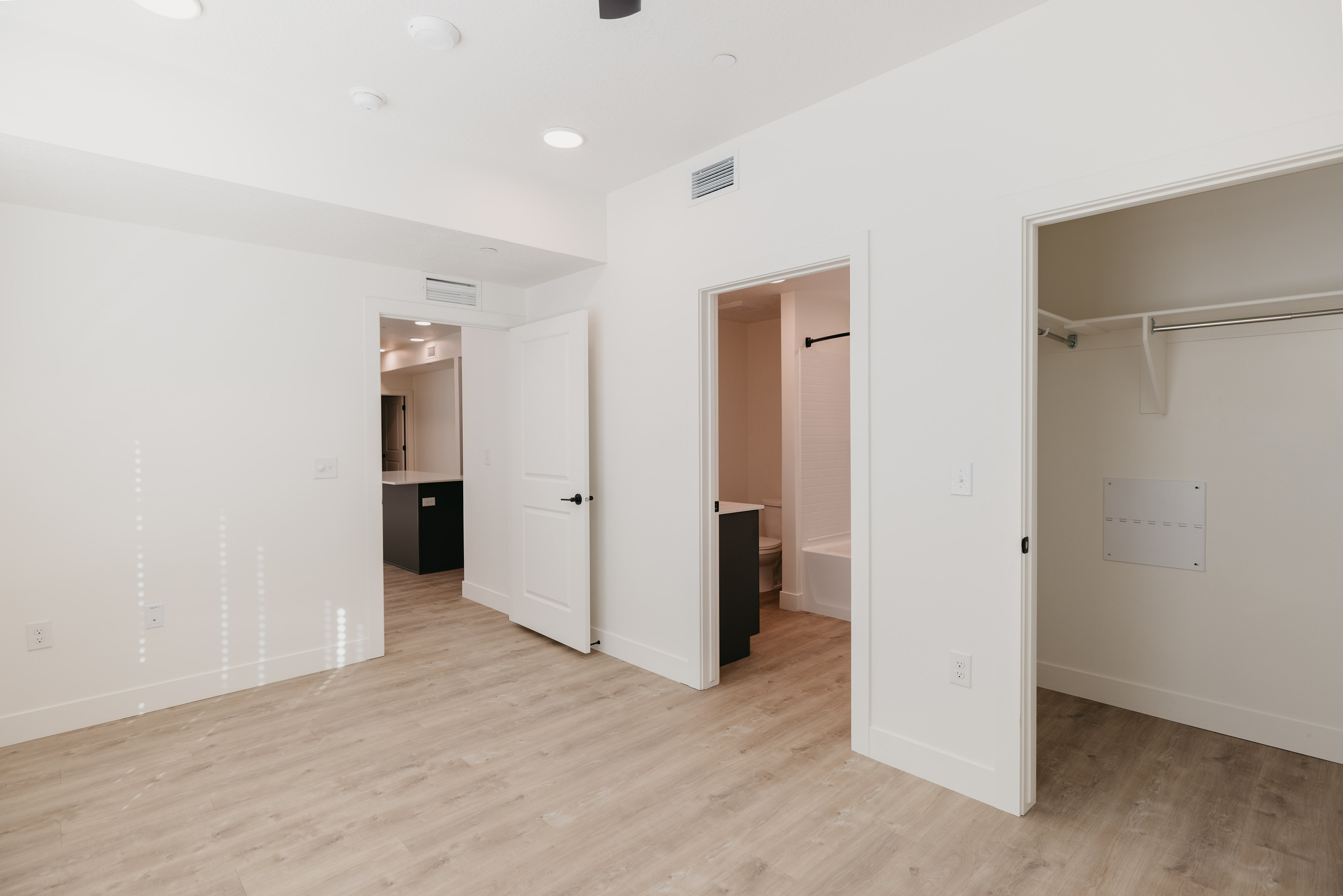 Bright and modern apartment interior with sleek hardwood floors, spacious closet, and a well-lit bathroom view.