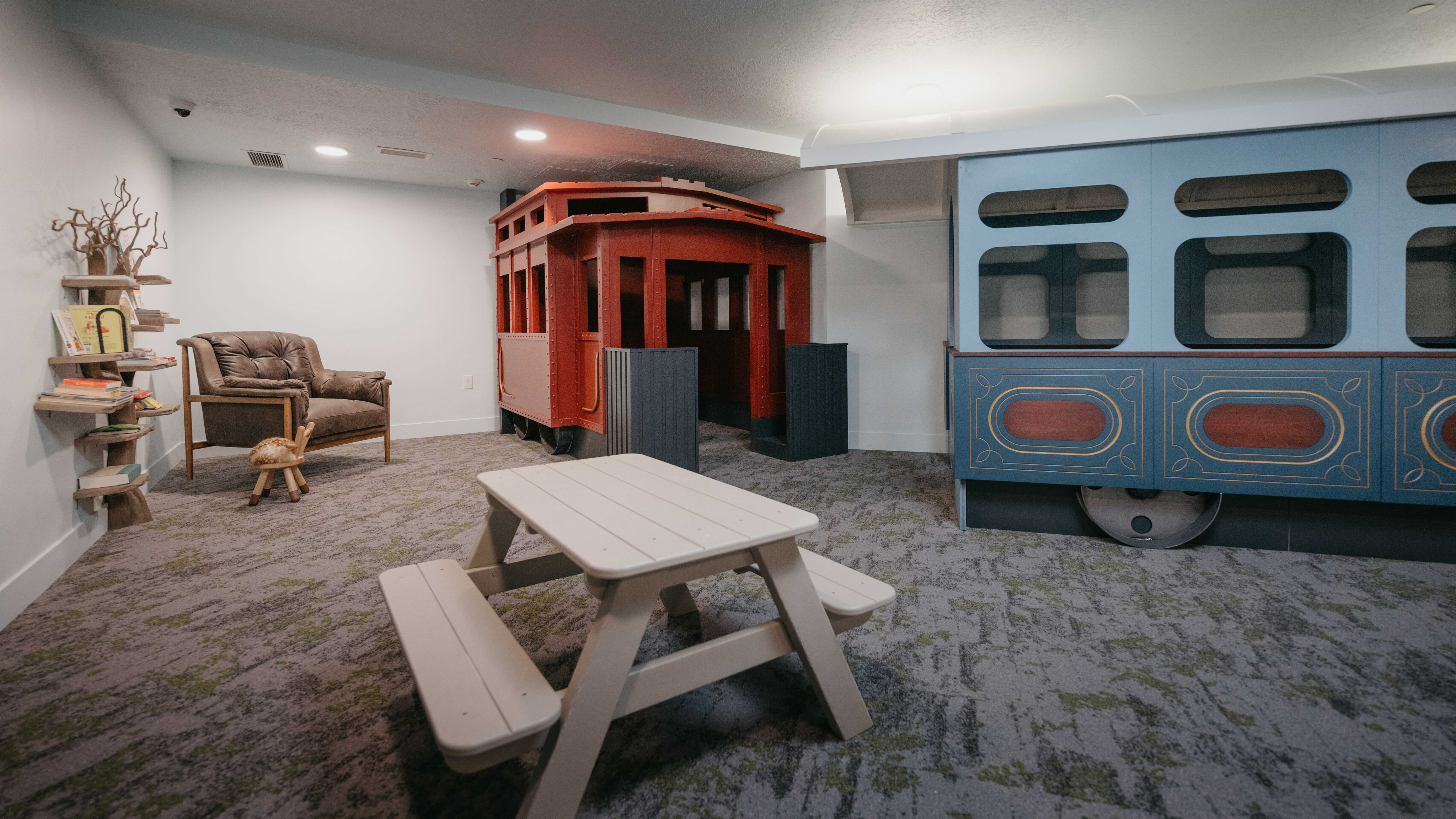 Inviting playroom with a charming vintage train theme, featuring cozy seating, a creative bookshelf, and a kid-friendly picnic table.