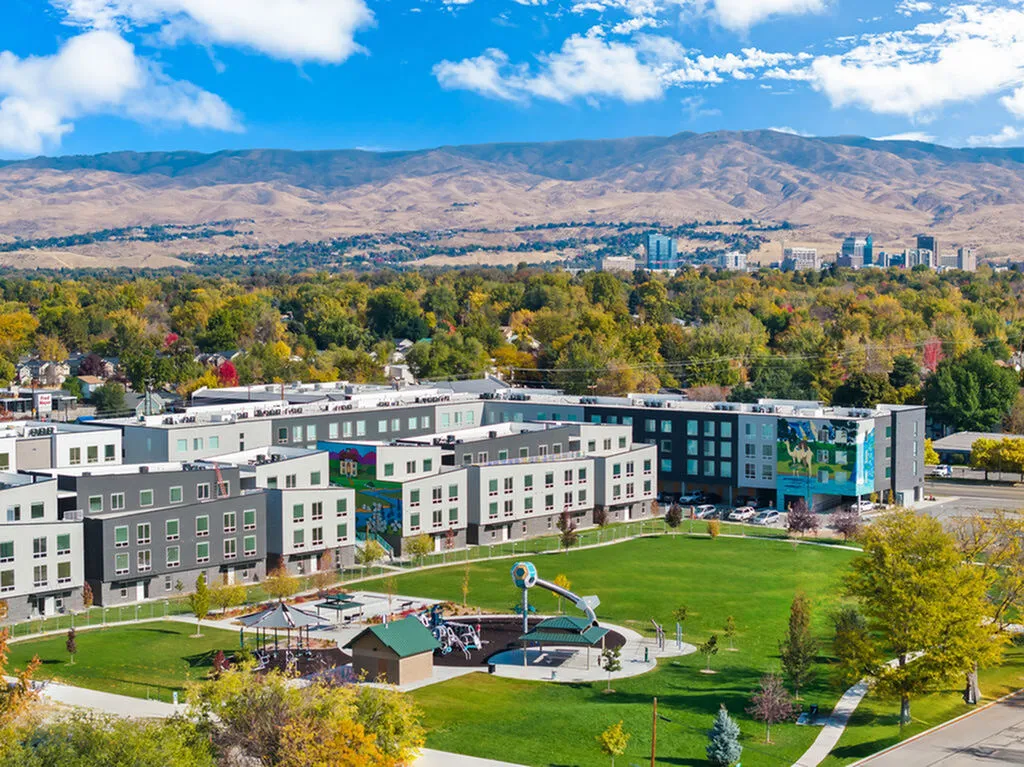 Vibrant apartment complex with modern design, nestled in lush green surroundings with stunning mountain views and a lively playground.