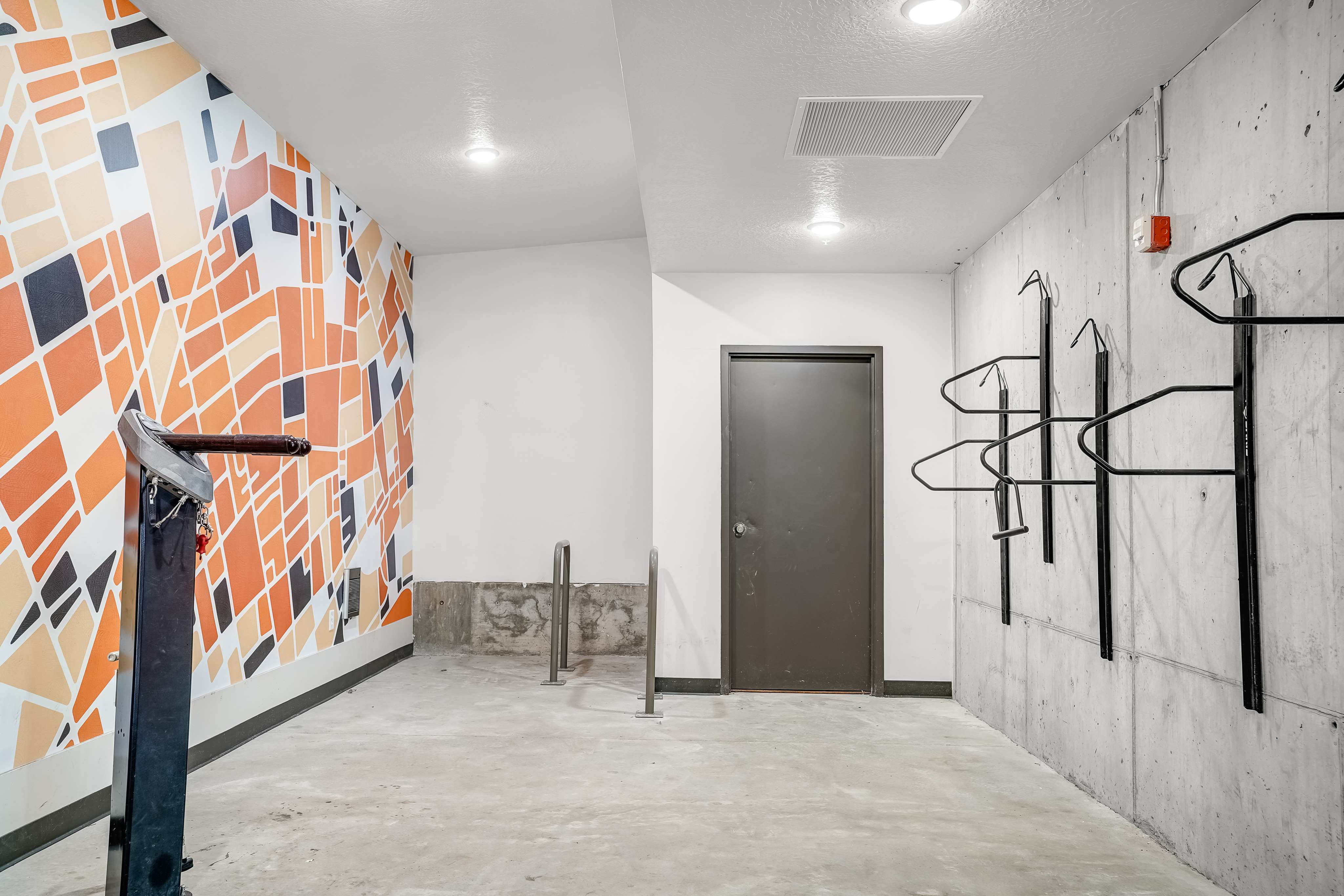 Chic urban bike storage area with vibrant geometric mural, sleek metal racks, and modern concrete design.
