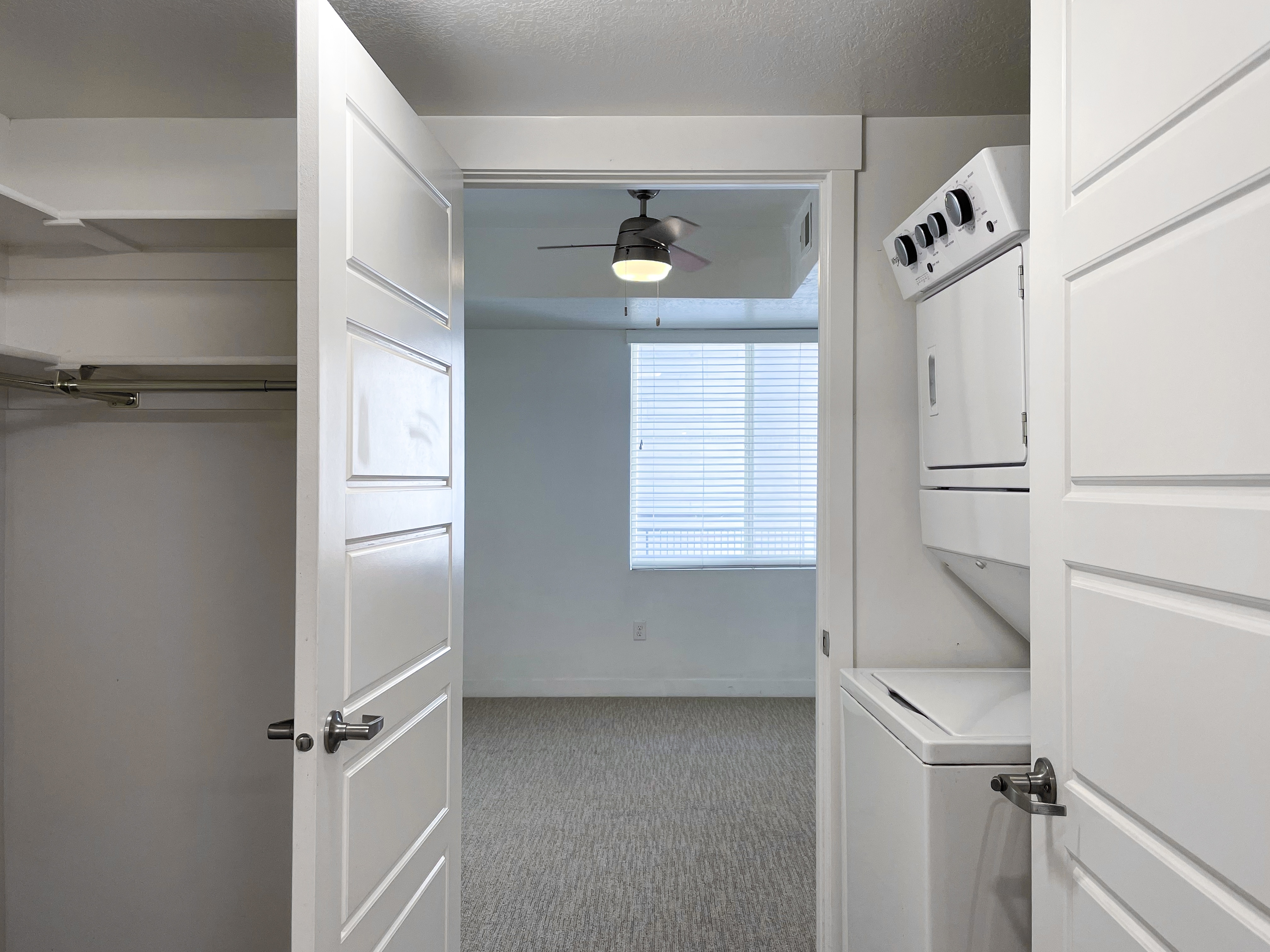 Modern apartment hallway showcasing in-unit laundry and spacious closet, filled with natural light from a large window.