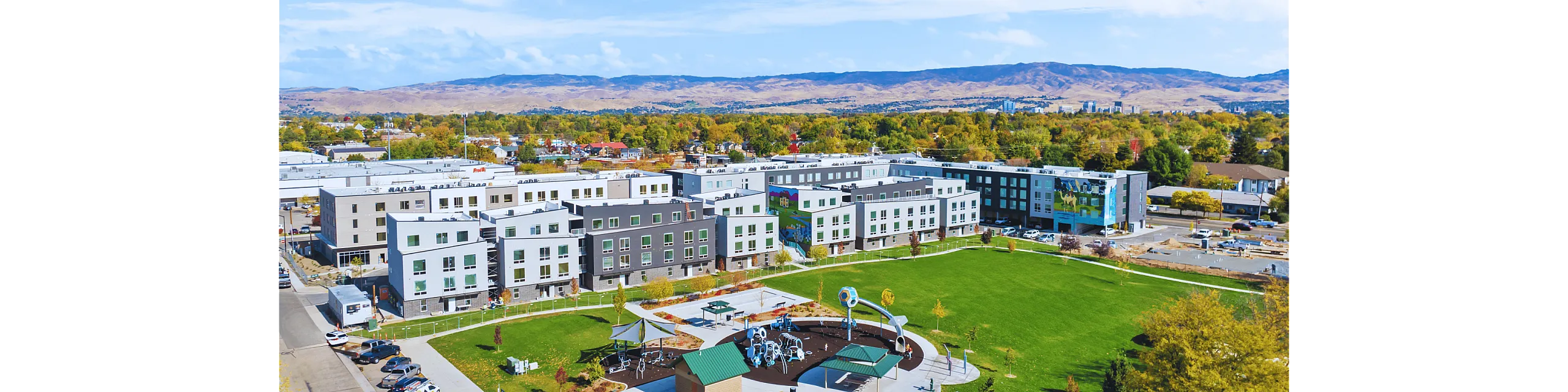 Aerial view of a modern apartment complex surrounded by lush greenery and a scenic landscape.