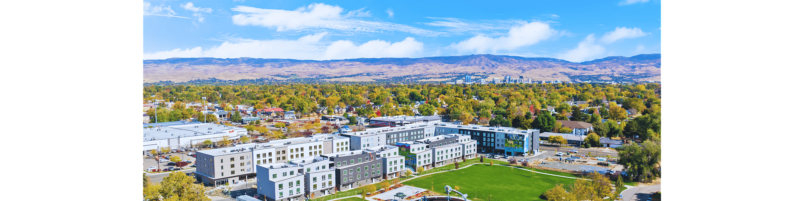 Aerial view of a modern apartment complex surrounded by lush greenery and scenic mountains.