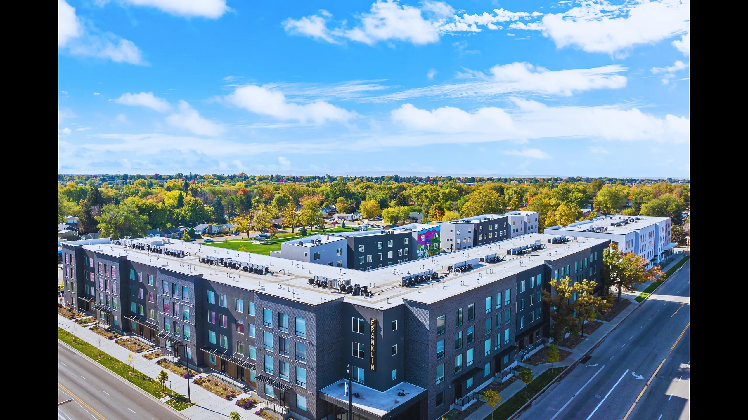 Aerial view of a modern apartment complex surrounded by lush greenery and a vibrant neighborhood.