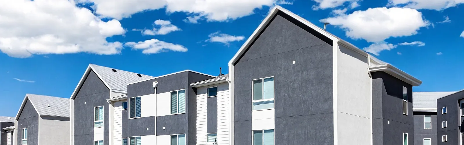Modern townhouse complex under a vibrant blue sky, featuring well-maintained landscaping and a stylish exterior.