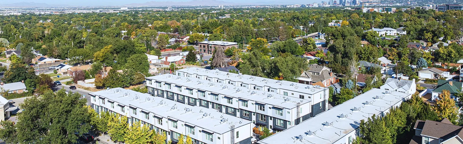 Aerial view of modern apartment complex surrounded by lush greenery and cityscape in the background.