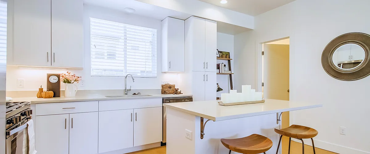 Bright and welcoming kitchen with a minimalist design, featuring white cabinetry, a cozy breakfast bar with stools, and soft lighting.