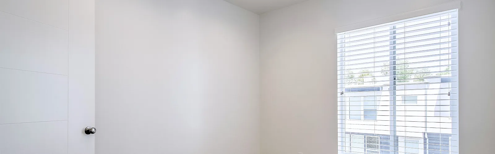 Bright and airy bedroom with soft carpet, large window with blinds, and modern lighting.