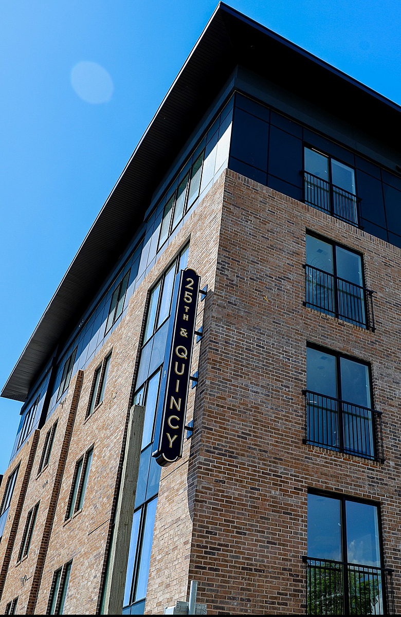 Modern apartment building with sleek brick facade and large windows at 25th & Quincy, under a clear blue sky.
