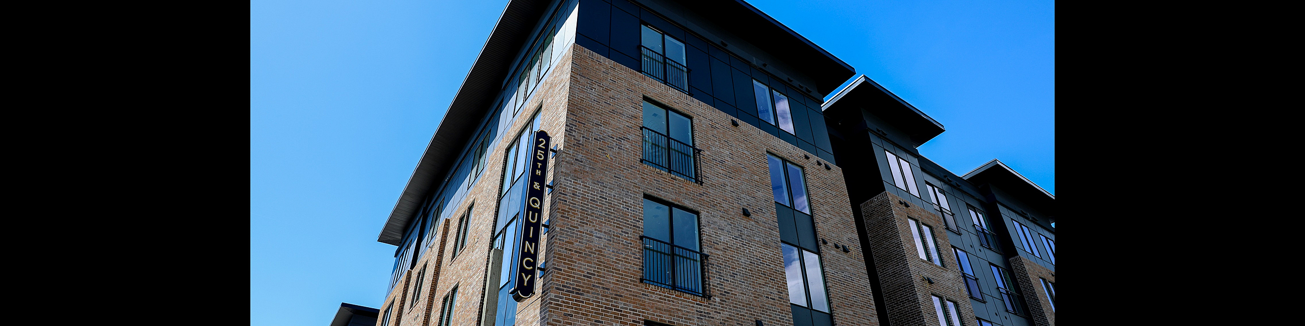 Modern apartment building with brick facade and large windows at 25th & Quincy, showcasing contemporary urban living.