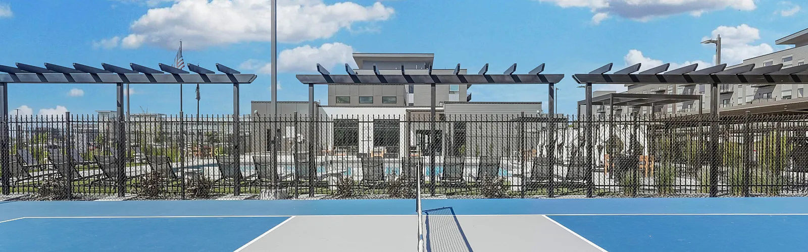 Vibrant tennis court in a modern apartment complex under a bright blue sky with fluffy clouds, showcasing lifestyle amenities.
