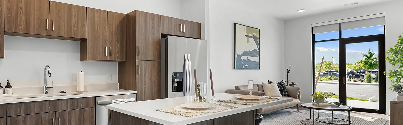 Modern apartment with sleek kitchen, stylish island seating, and a bright, open living room featuring large windows with a scenic view.