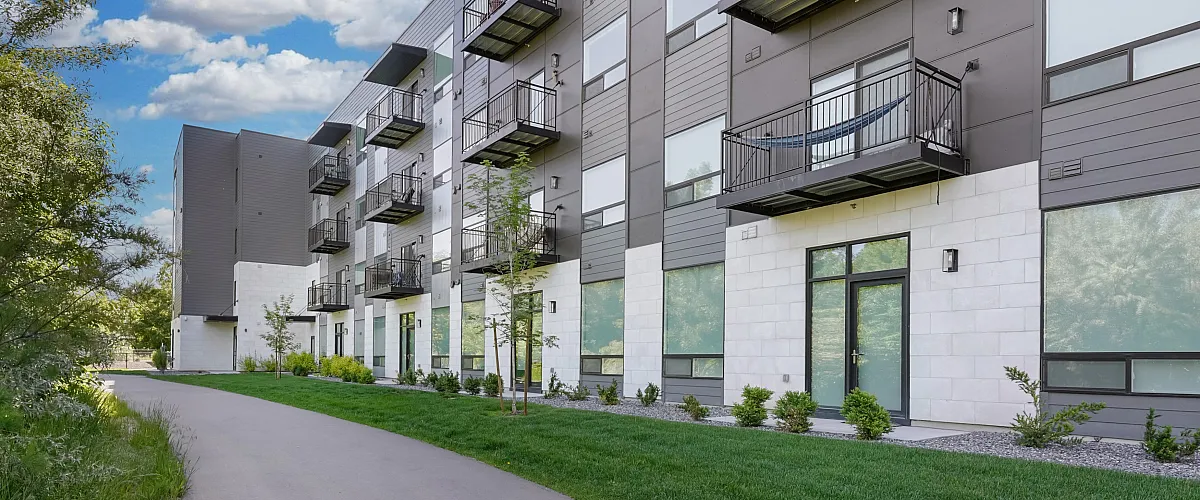 Modern apartment building with lush green surroundings, offering private balconies and scenic walking path.