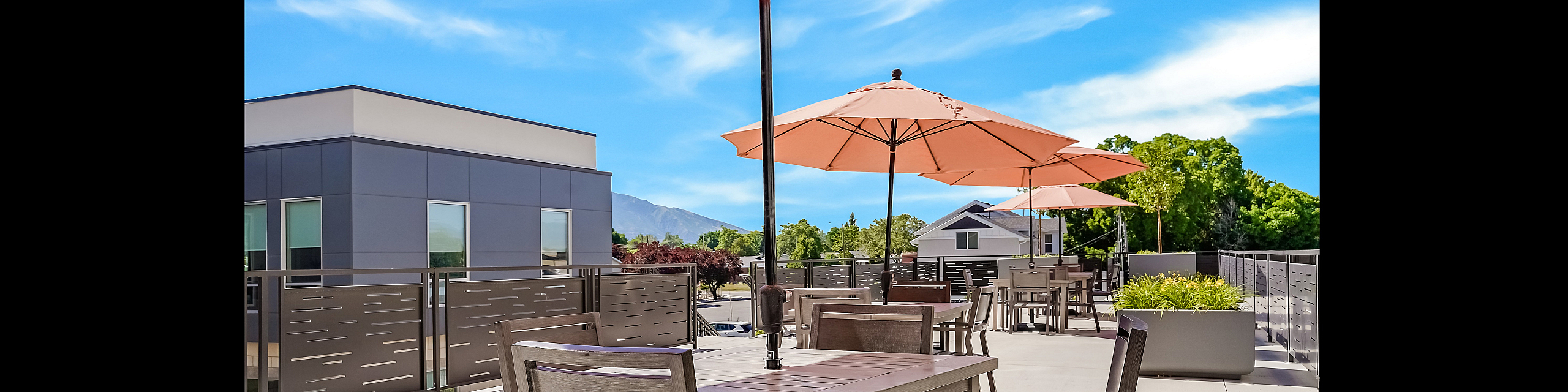 Chic outdoor terrace with modern dining sets under vibrant umbrellas, framed by lush greenery and stunning mountain views.