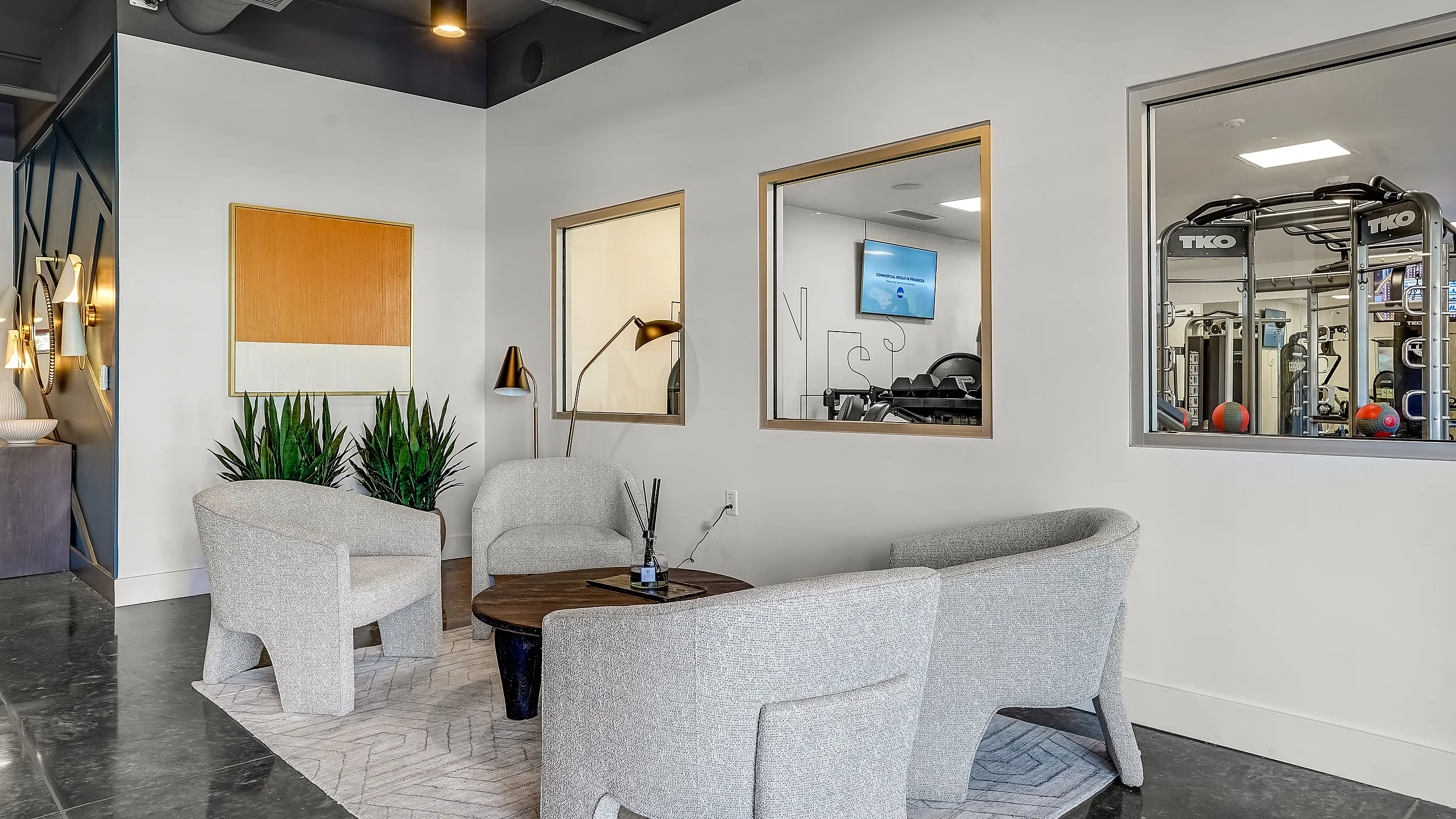 Modern lounge area with stylish chairs, contemporary decor, and a view into a state-of-the-art gym facility.
