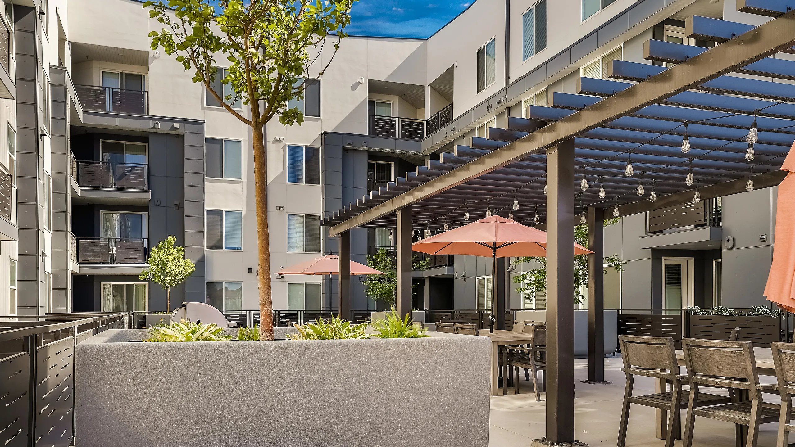 Contemporary apartment courtyard with stylish pergola, chic dining area, and vibrant greenery for social relaxation.