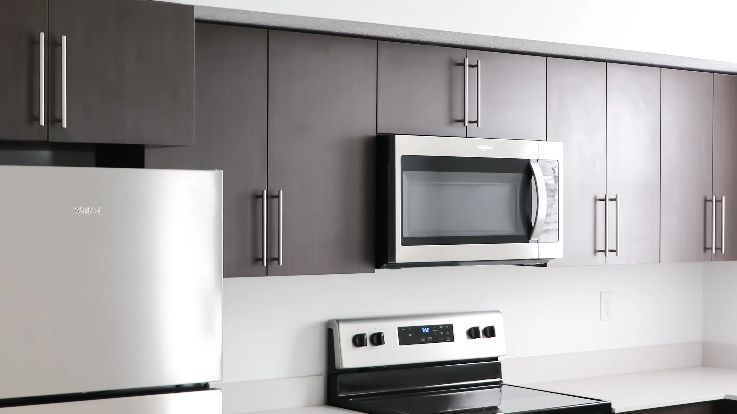 Sleek modern kitchen with stainless steel appliances, dark wood cabinets, and smooth countertops.