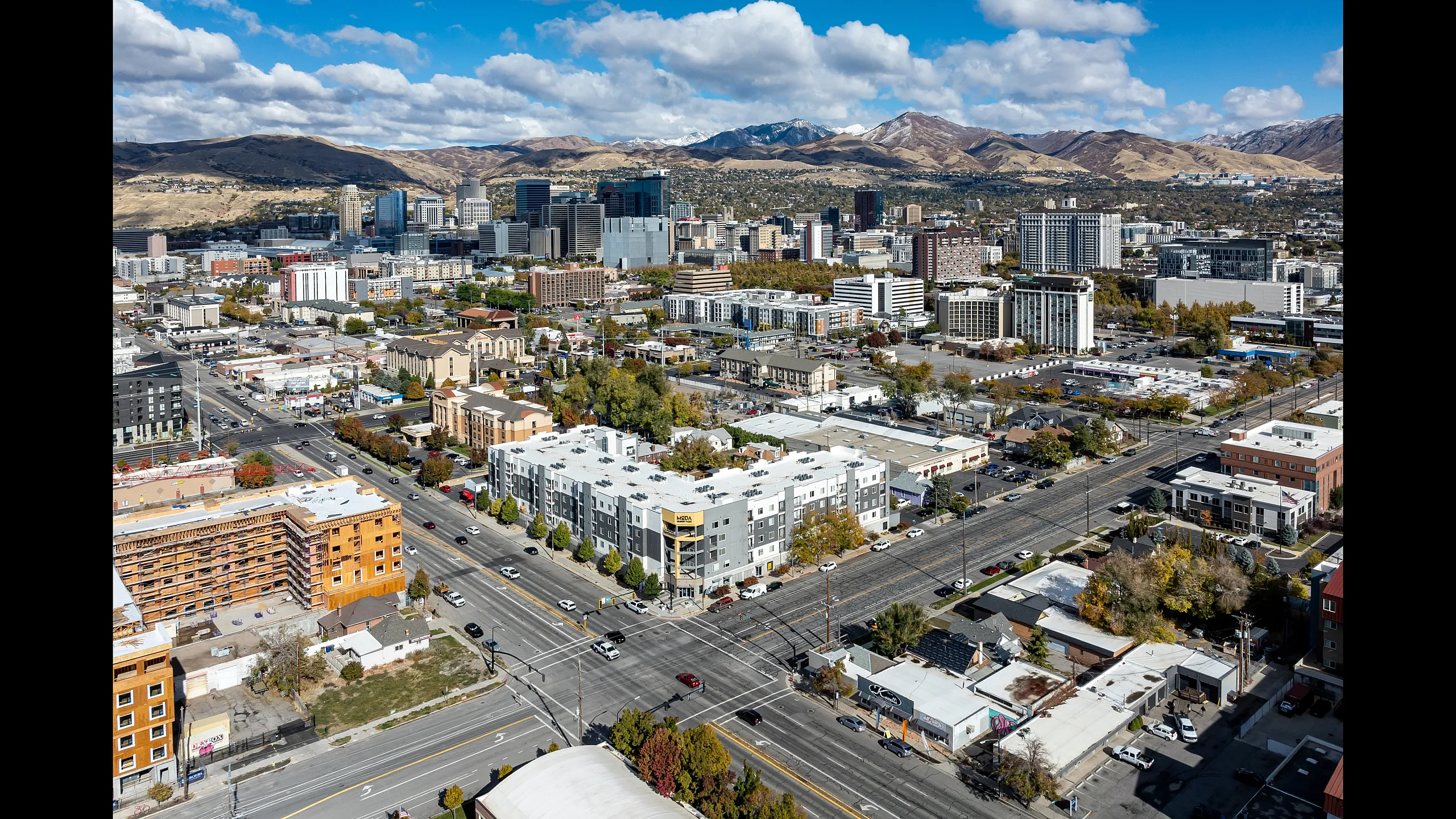 Stunning urban aerial view showcasing bustling cityscape, with modern architecture and scenic mountainous backdrop under a vibrant blue sky.