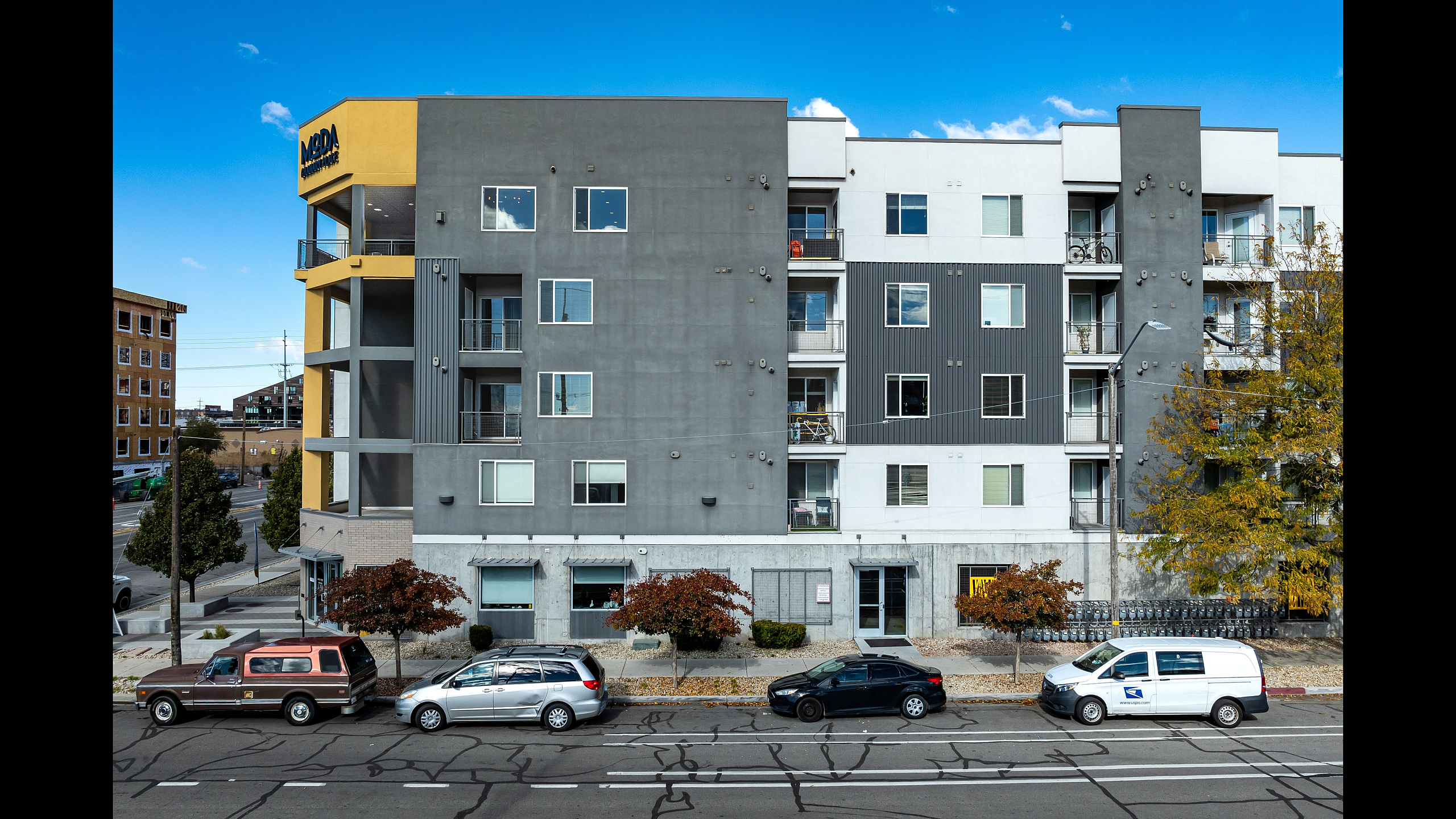 Modern apartment building with stylish exterior, featuring multiple balconies and large windows, set in a vibrant urban location with convenient street parking.