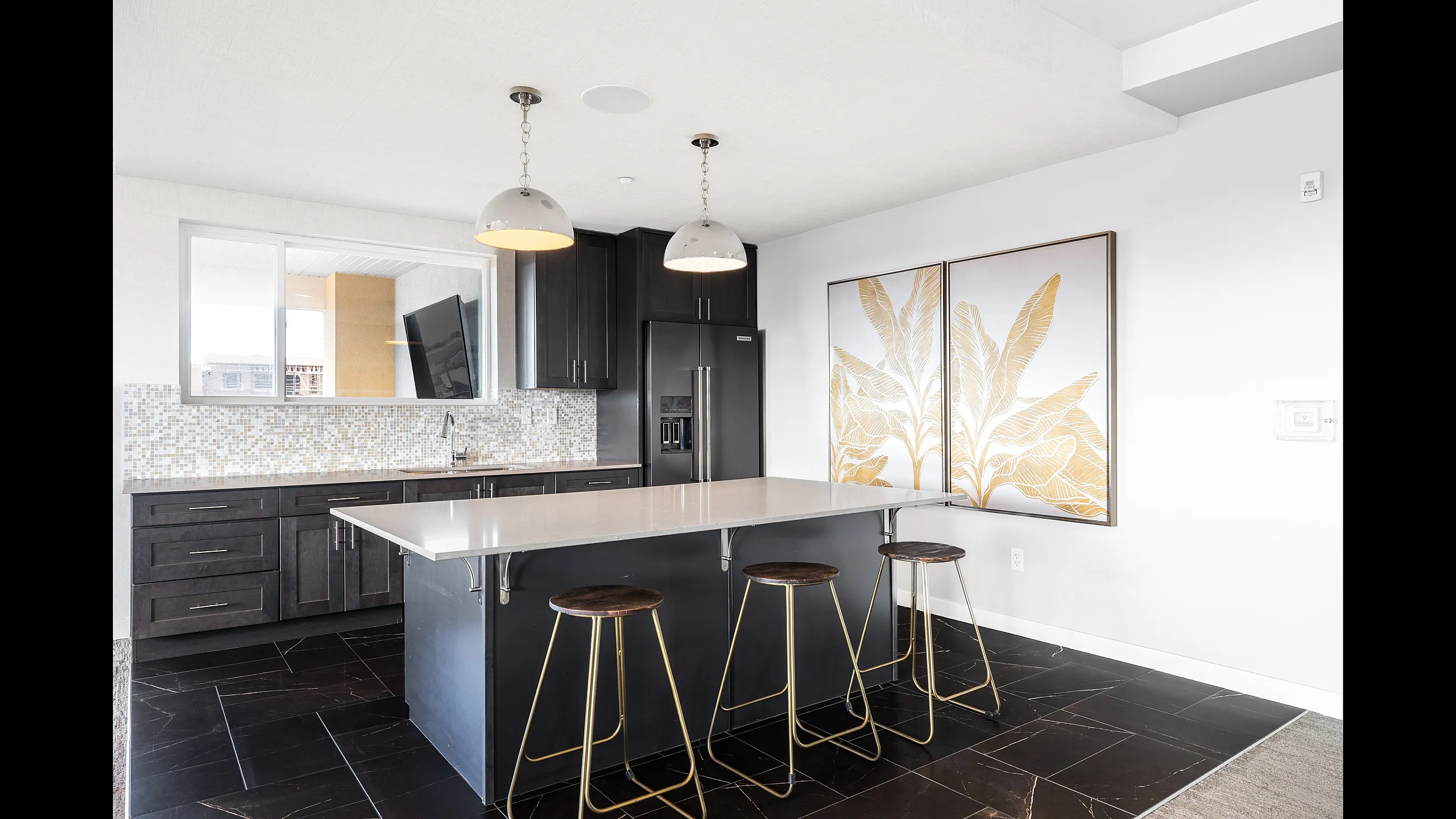 Elegant modern kitchen with dark wood cabinets, sleek island with bar stools, and stylish gold leaf artwork enhancing the bright, open space.