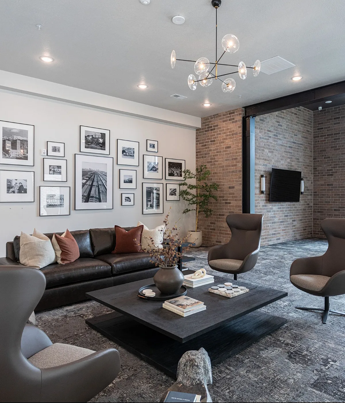 Luxurious lounge area featuring a contemporary leather sofa, modern armchairs, and an eye-catching photo gallery wall, illuminated by elegant pendant lighting and large windows.