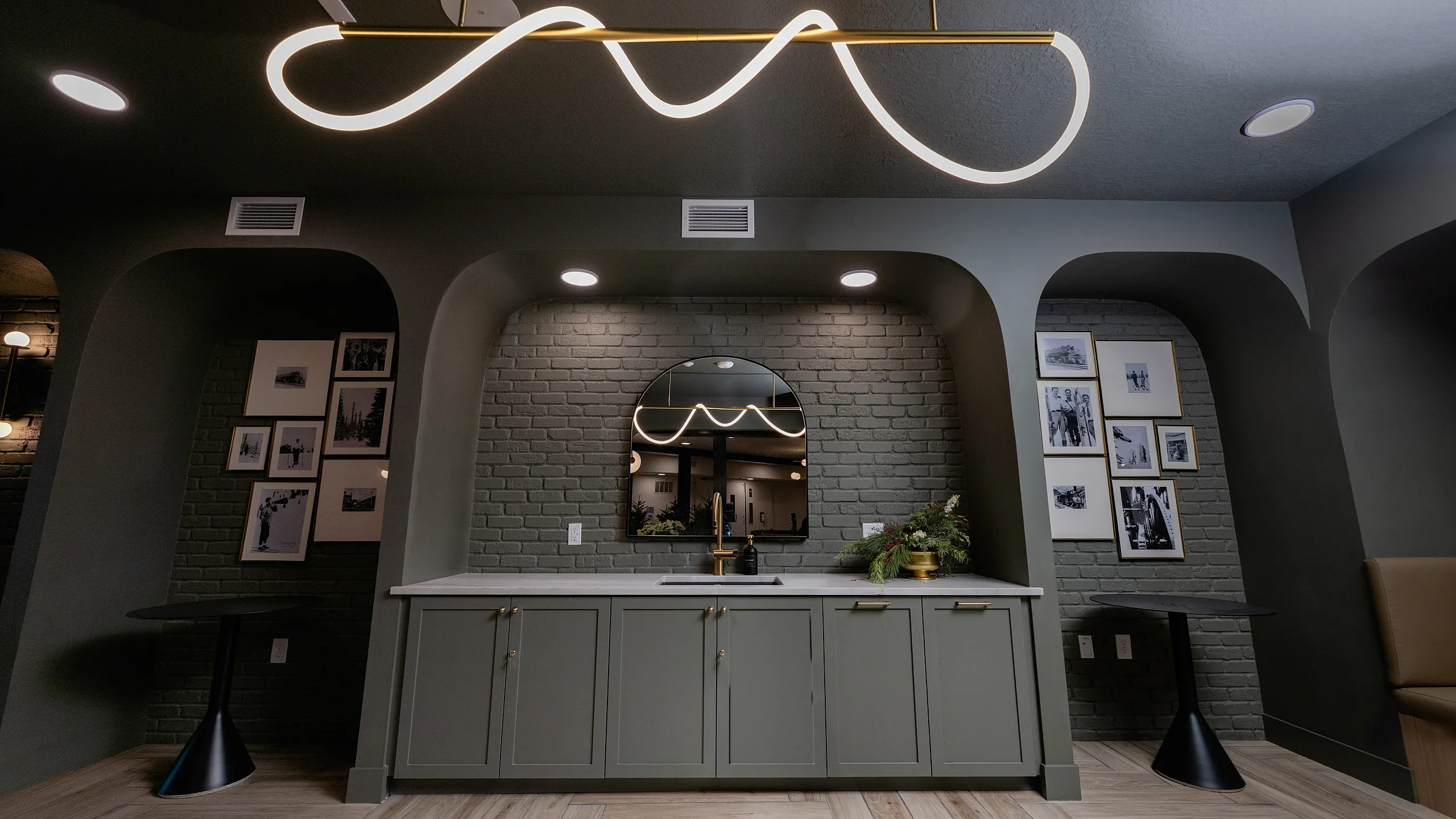 Elegant modern living space with chic lighting, arched brick walls, stylish cabinetry, and curated photo gallery.
