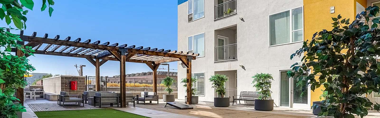 Chic apartment building with vibrant blue and yellow accents, featuring a lush courtyard with modern seating and pergola.