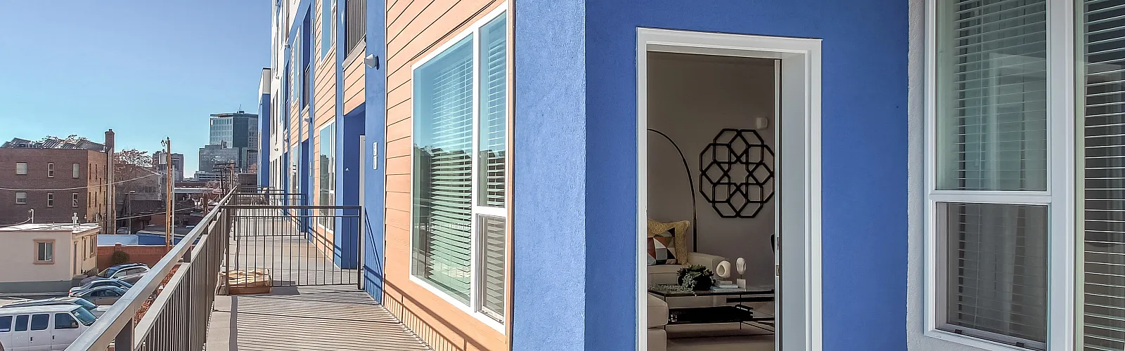 Modern apartment exterior with vibrant blue and wood paneling, featuring a spacious balcony and inviting interior glimpses.