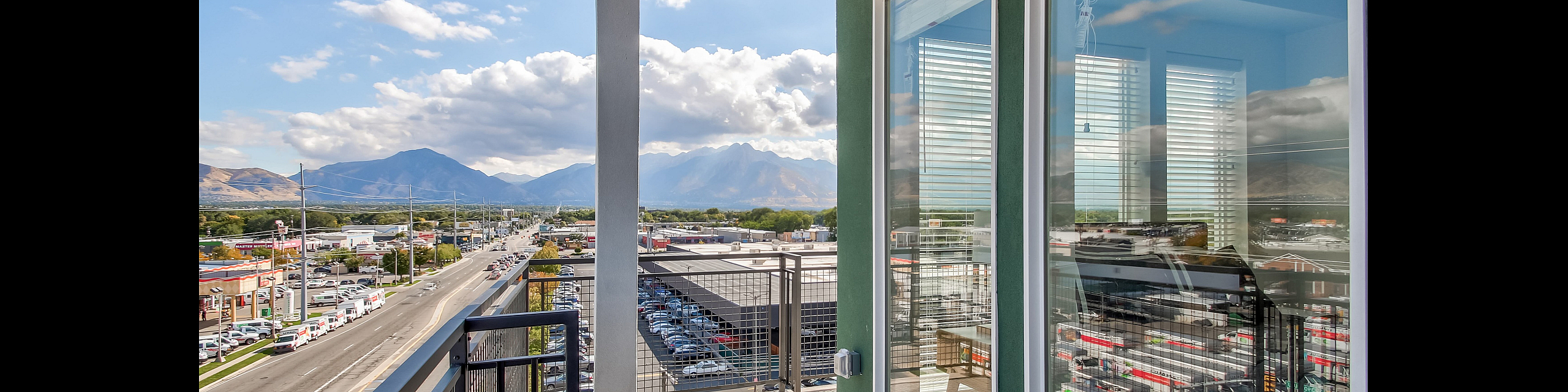 Charming apartment balcony with breathtaking mountain views and vibrant cityscape, featuring modern green exterior and large reflective windows.