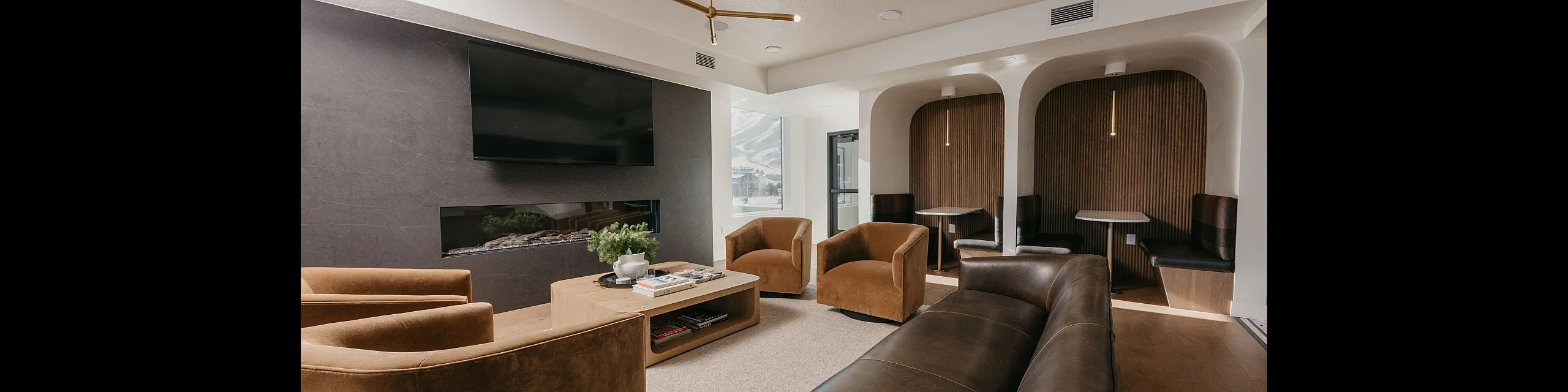 Elegant living room with modern fireplace, sleek TV setup, and plush seating, featuring cozy alcove dining nooks with wood accents.