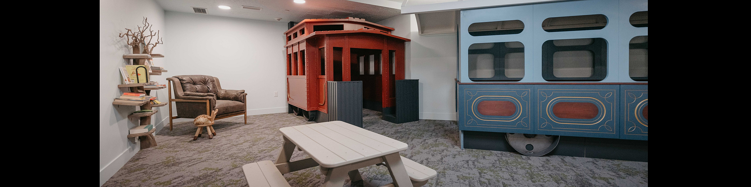 Charming playroom featuring a whimsical train structure, cozy reading corner, and child-sized picnic table, offering a playful and inviting space.