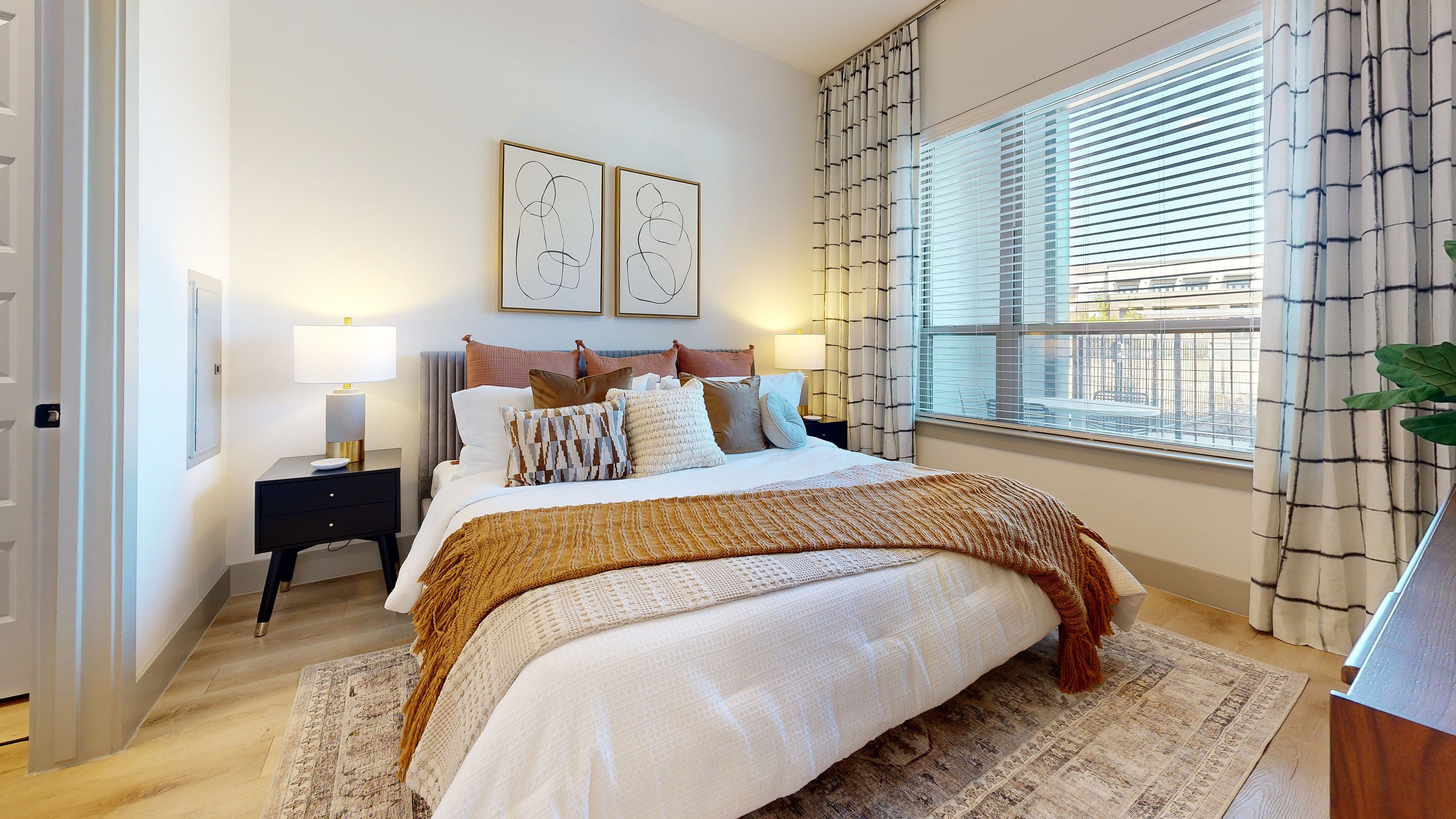 A bedroom featuring a cozy bed, chic decor, a large window offering ample natural light, and hardwood-style flooring.