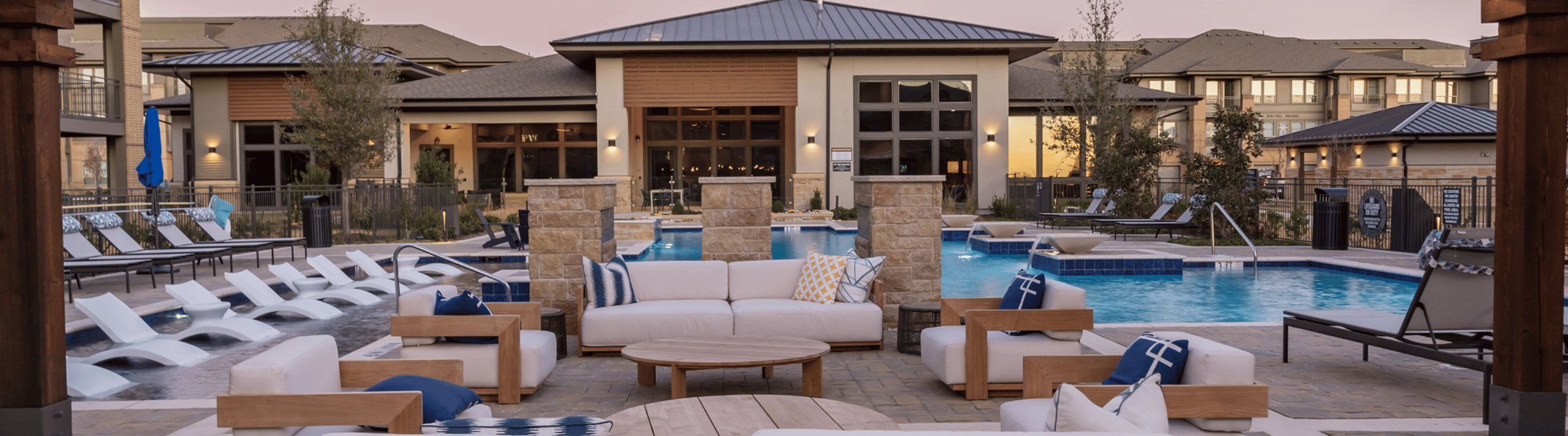 Chic apartment complex with a modern pool bordered by stylish loungers and cozy seating areas at sunset.