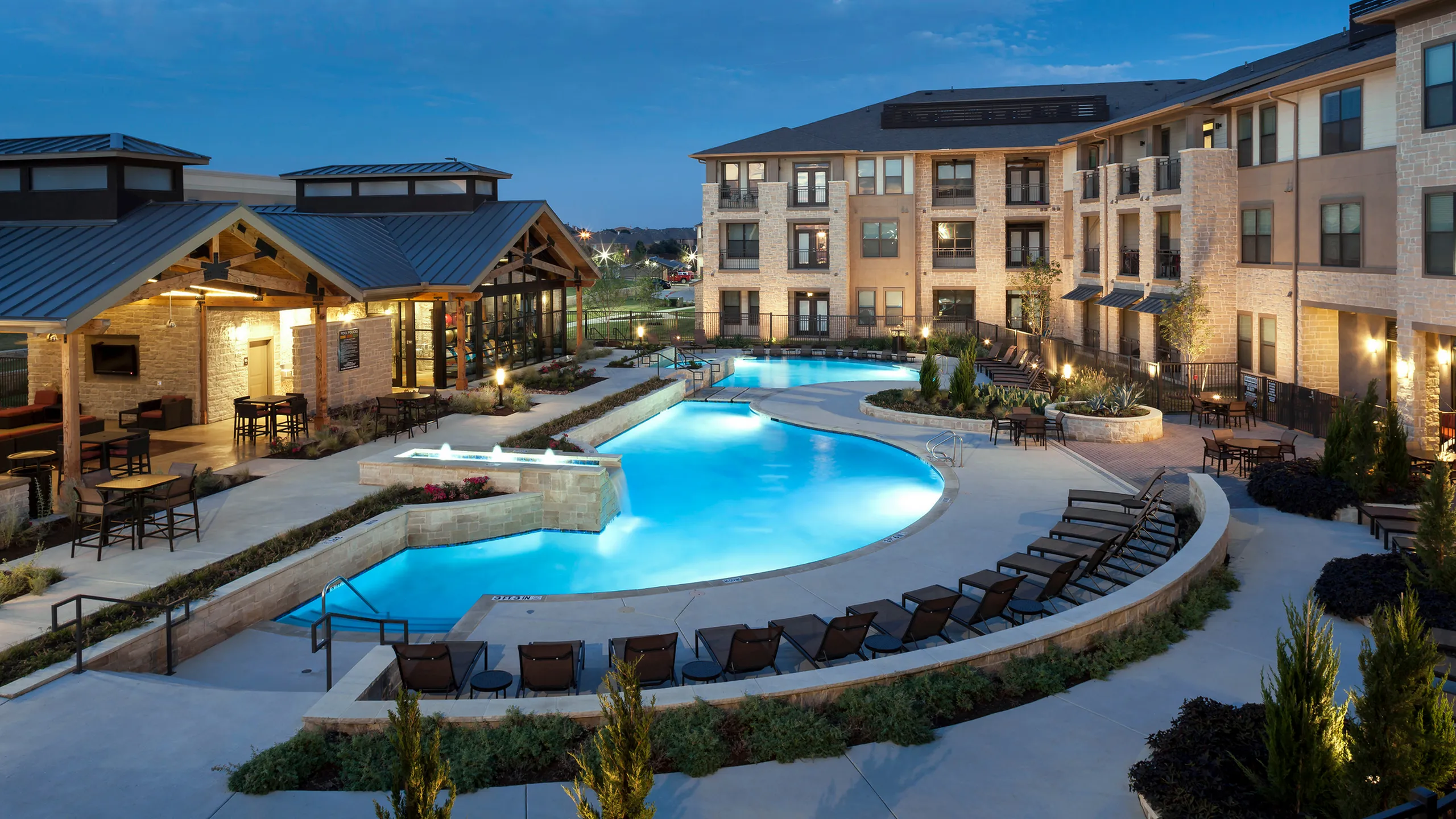 Inviting pool area in a modern apartment complex, with lounge chairs and well-lit surroundings.