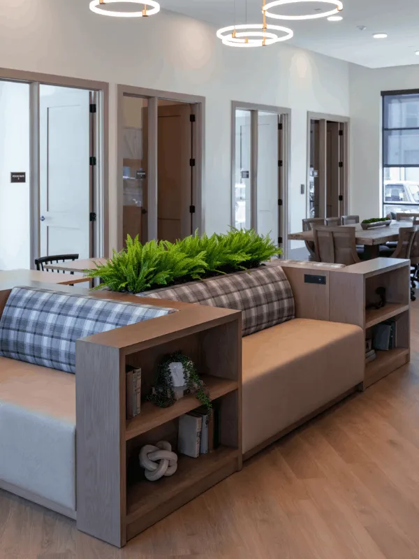 Modern lounge area with stylish plaid seating, wooden shelving, and vibrant green plants, complemented by elegant circular ceiling lights and a spacious layout at Harvest House in Argyle.
