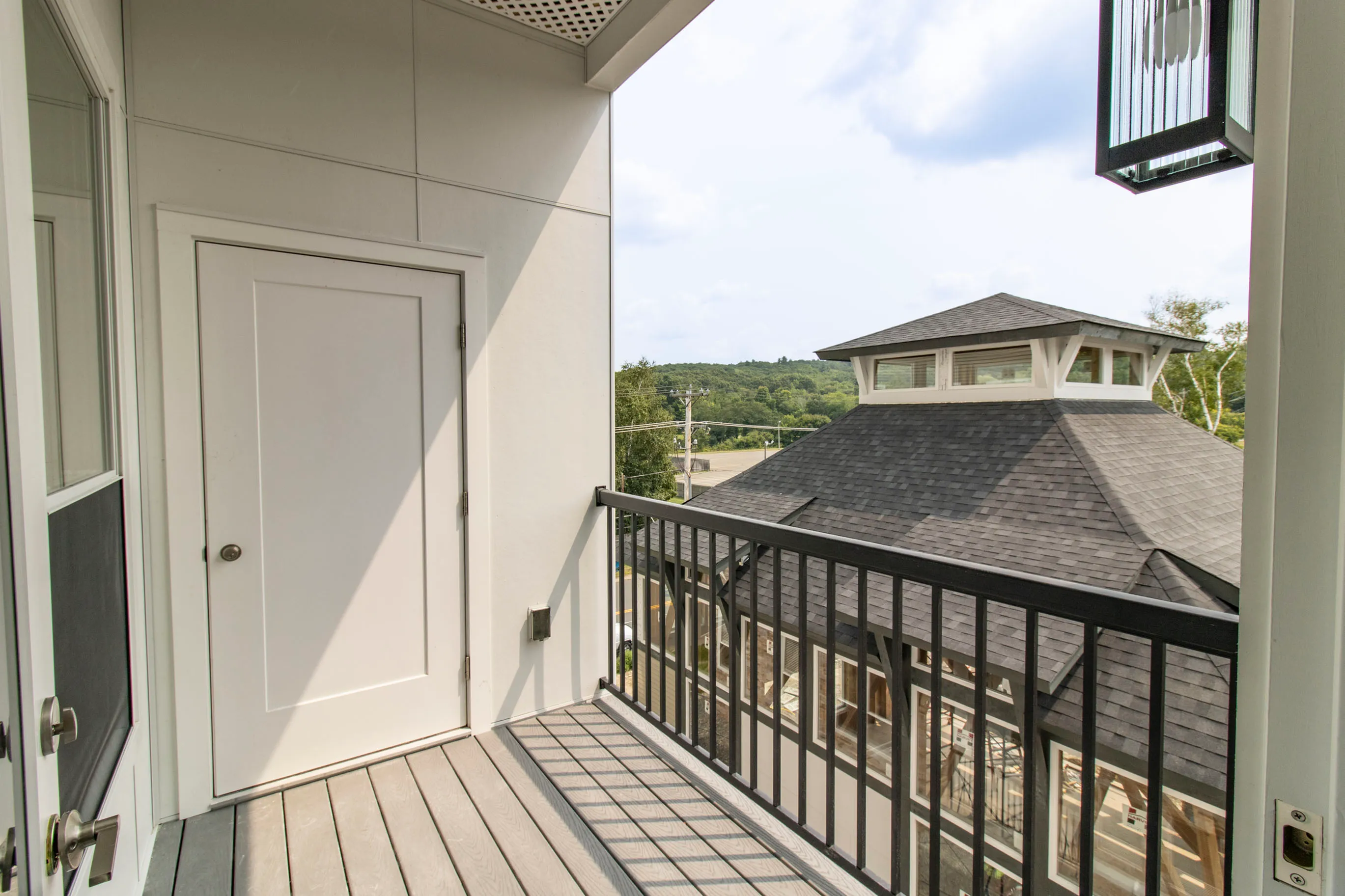 The James Apartments | Balcony with a wooden floor, black railing, and a view of a rooftop pavilion, with a closed door leading into the apartment | Luxury Apartments in Haverhill MA