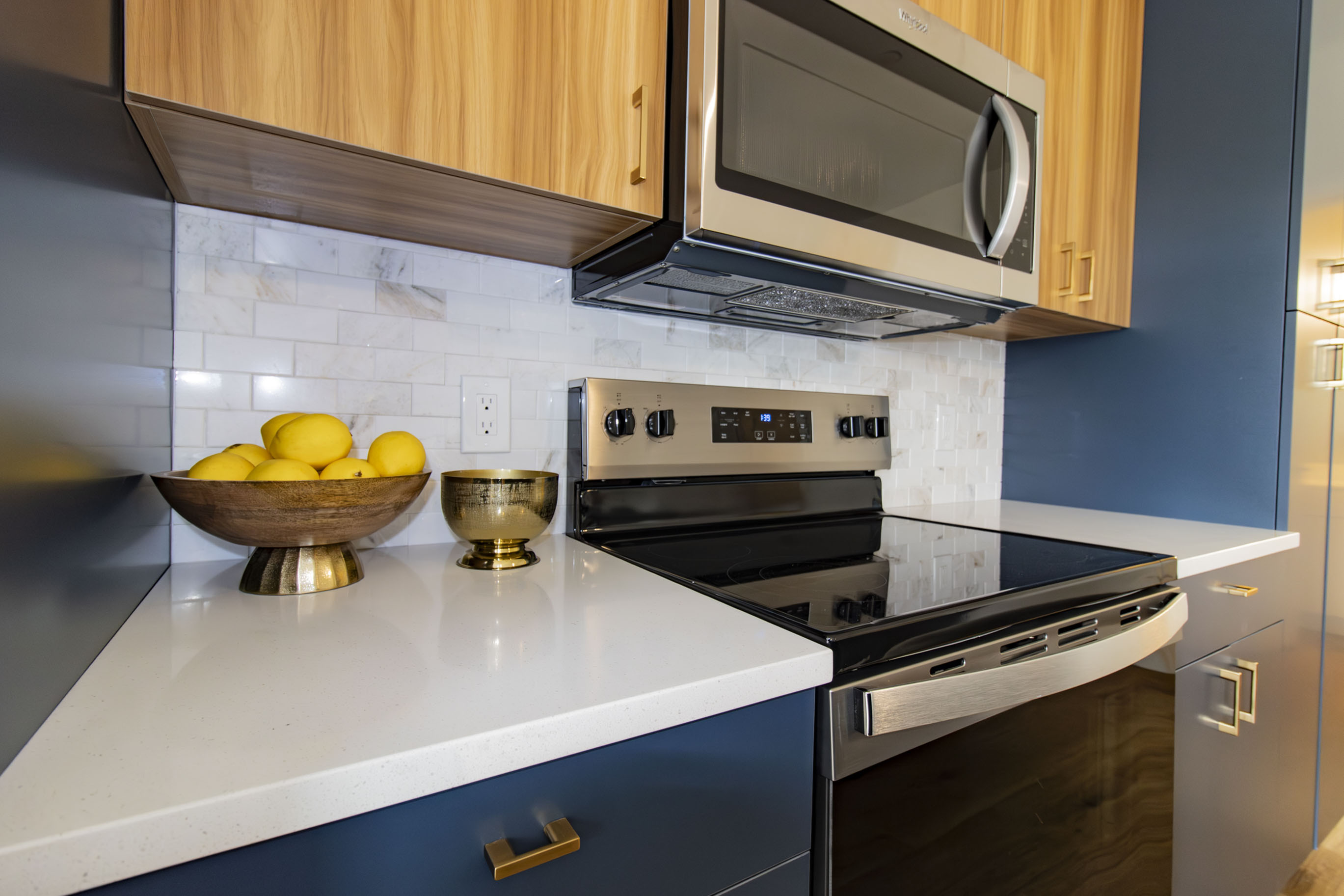 The James Apartments | Close-up of a modern kitchen stove and microwave with custom tile backsplash and decorative accents including a bowl of lemons and a brass bowl on the countertop | Luxury Apartments in Haverhill MA