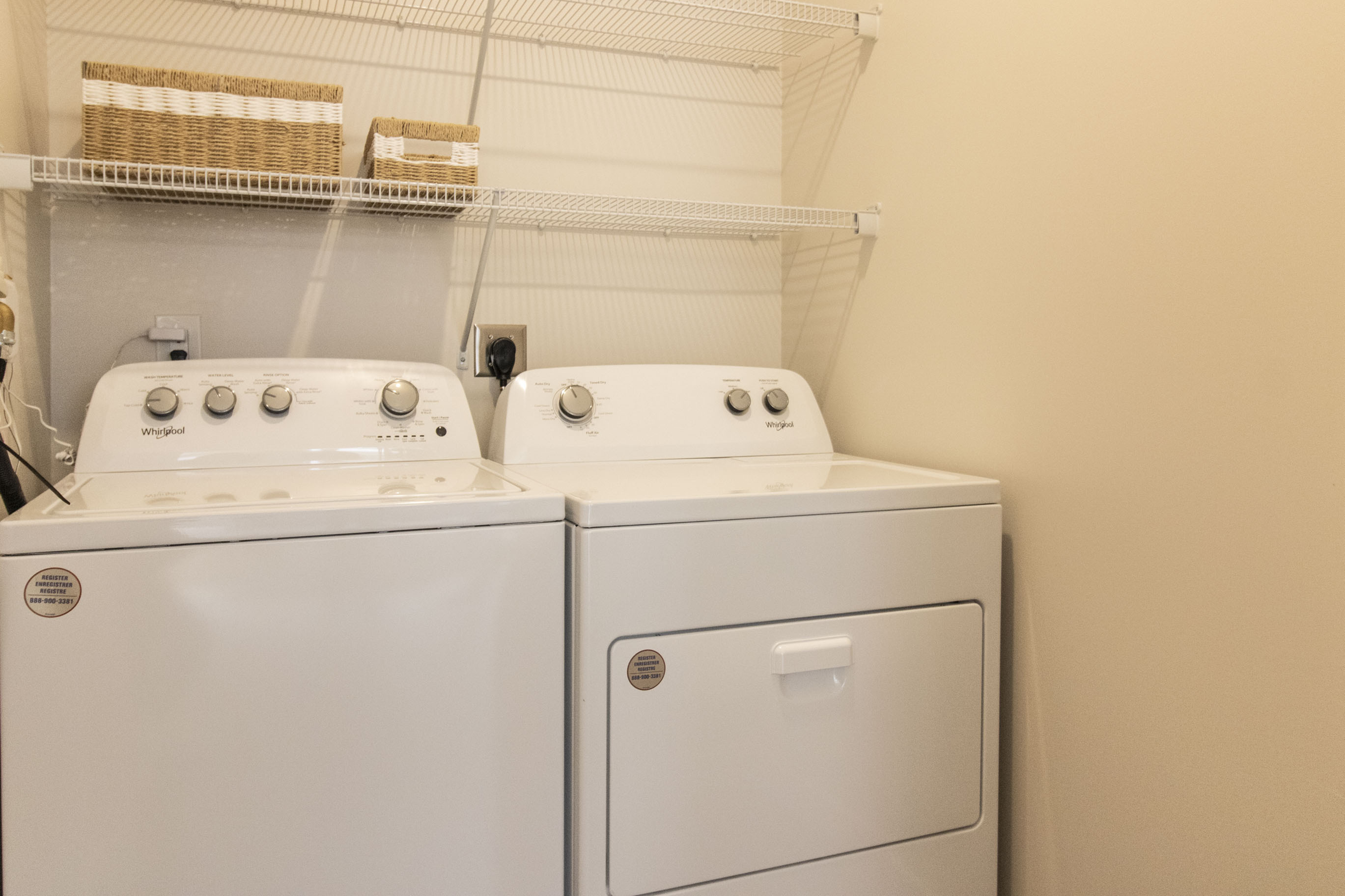The James Apartments | Laundry room with a matching white Whirlpool washer and dryer set under a wire shelf | Luxury Apartments in Haverhill MA