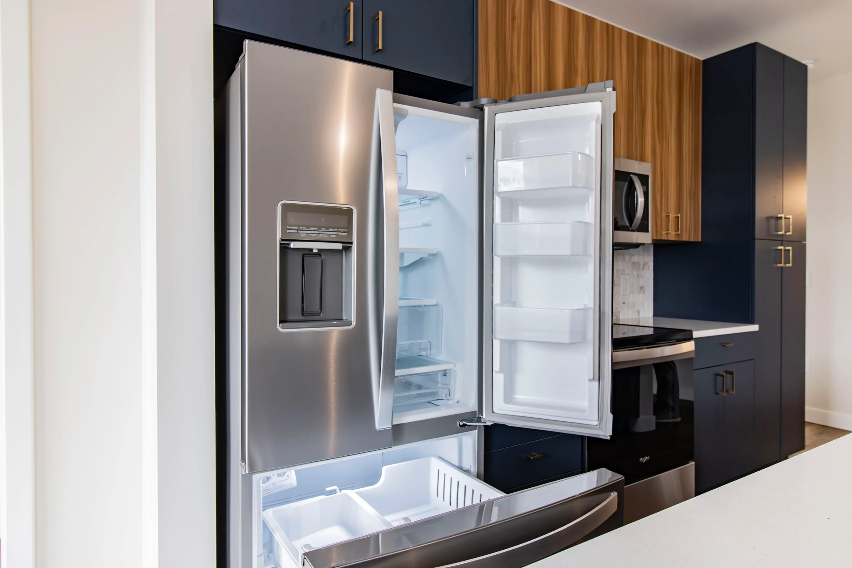 The James Apartments | Kitchen with an open stainless steel refrigerator, showing a well-organized space with adjacent dark blue and wooden cabinetry | Luxury Apartments in Haverhill MA