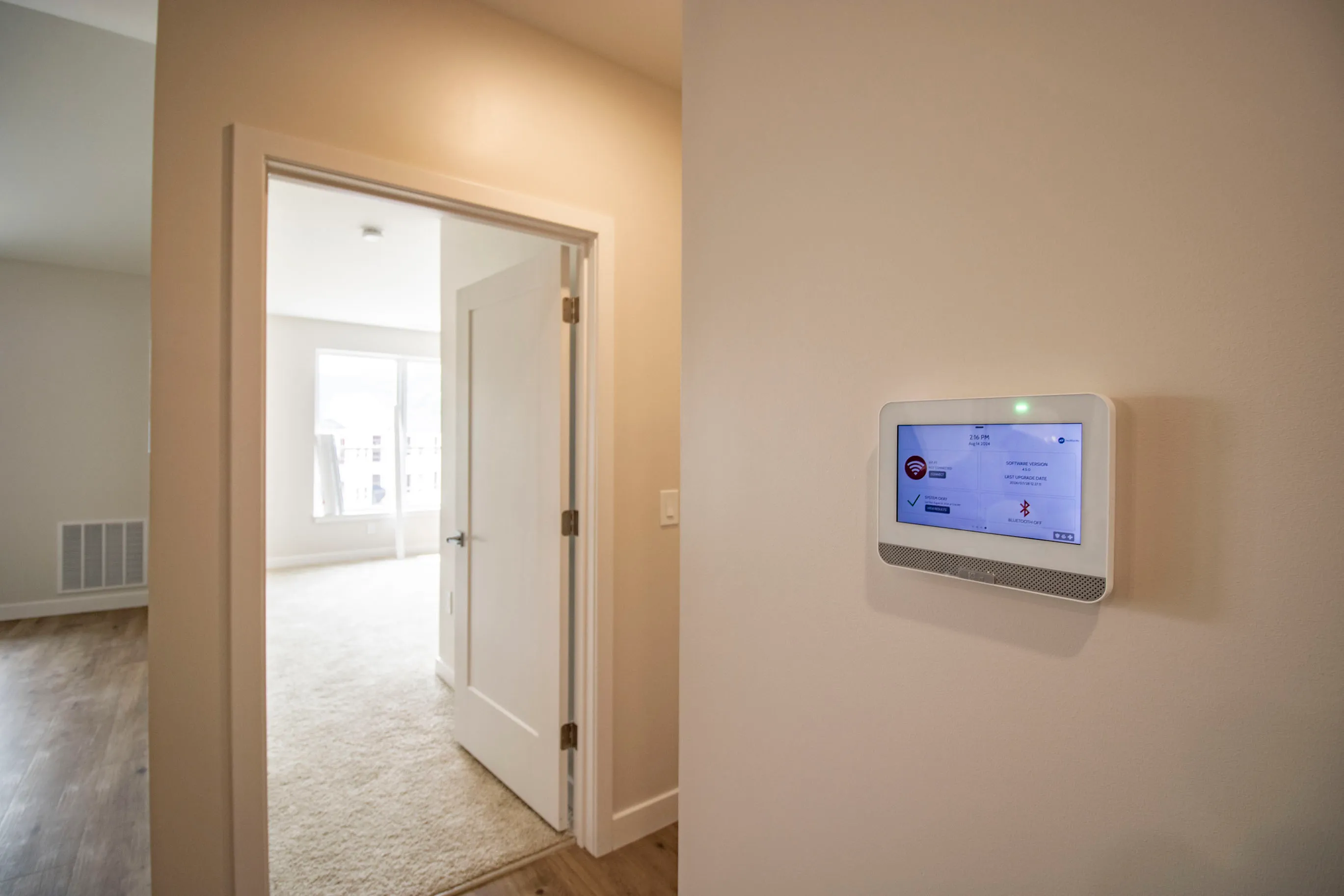 The James Apartments | Smart home ADT system panel mounted on the wall near a doorway, leading to a carpeted bedroom with natural light | Luxury Apartments in Haverhill MA
