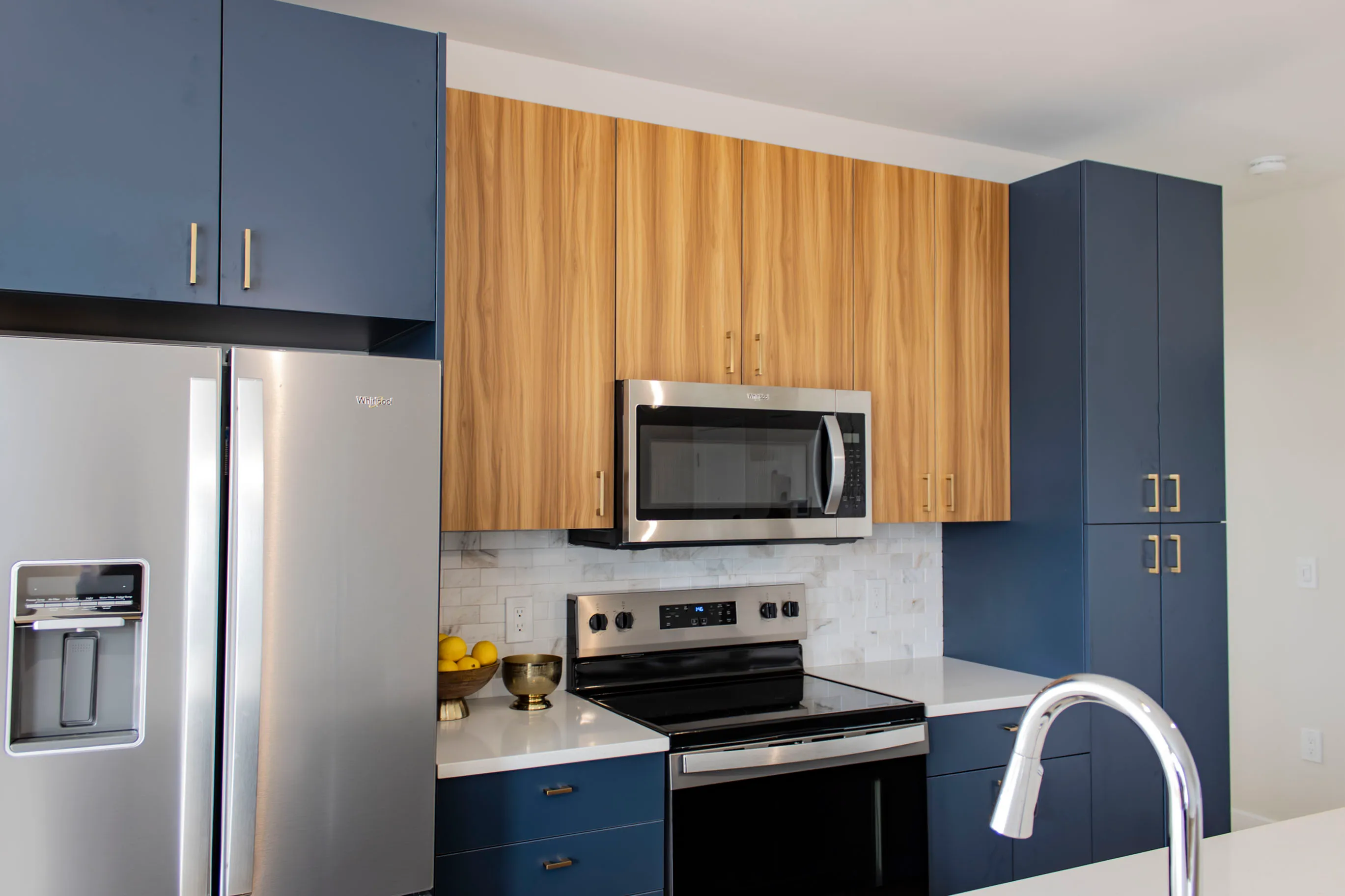 The James Apartments | Stainless Steel Modern kitchen with stainless steel appliances, including a double-door refrigerator and microwave, accented by dark blue and wooden cabinetry | Luxury Apartments in Haverhill MA