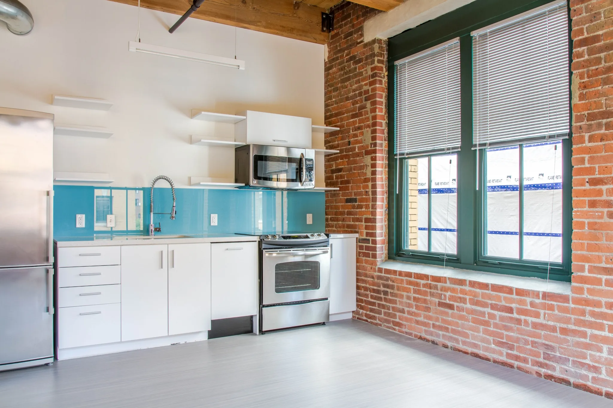 Contemporary loft kitchen with stainless steel appliances, exposed brick walls, and large windows.