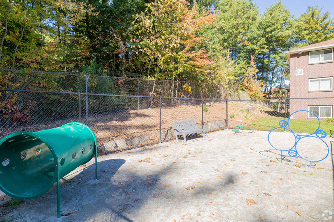 Sunny apartment dog park at Pheasant Run Apartments in Nashua NH  with agility equipment and seating area.