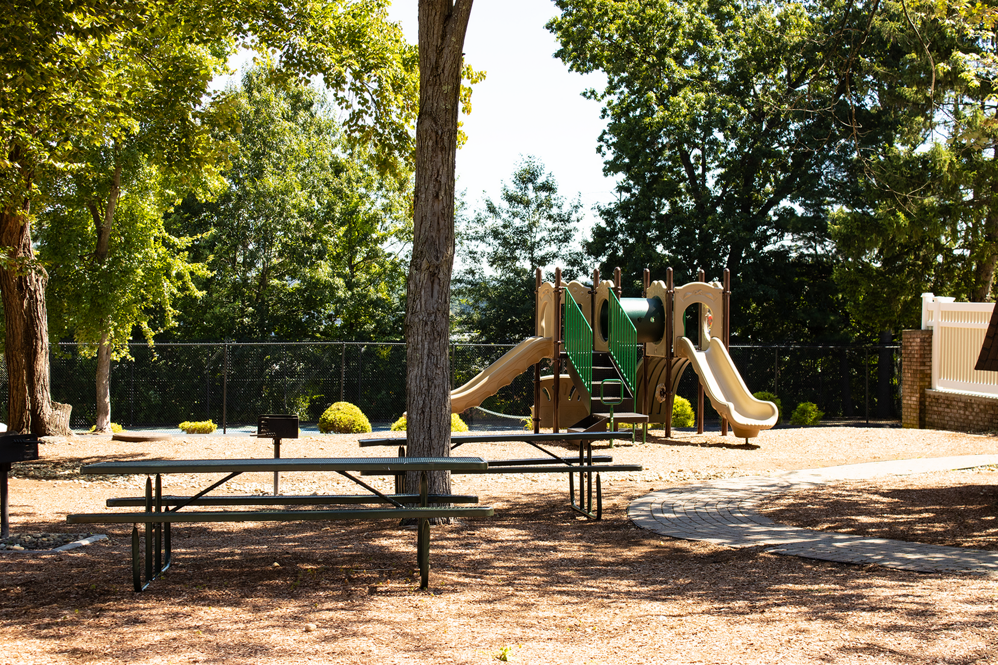 Charming playground area with slides and picnic tables under lush green trees.