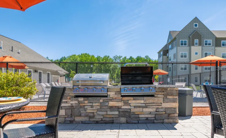 Charming outdoor BBQ area with modern grills, comfortable seating under vibrant orange umbrellas, and a backdrop of stylish apartment buildings.