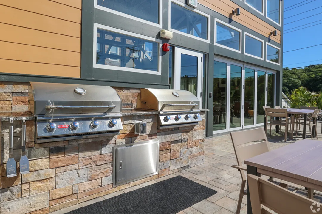 Modern outdoor patio featuring sleek built-in grills, elegant dining sets, and large glass doors, perfect for entertaining.
