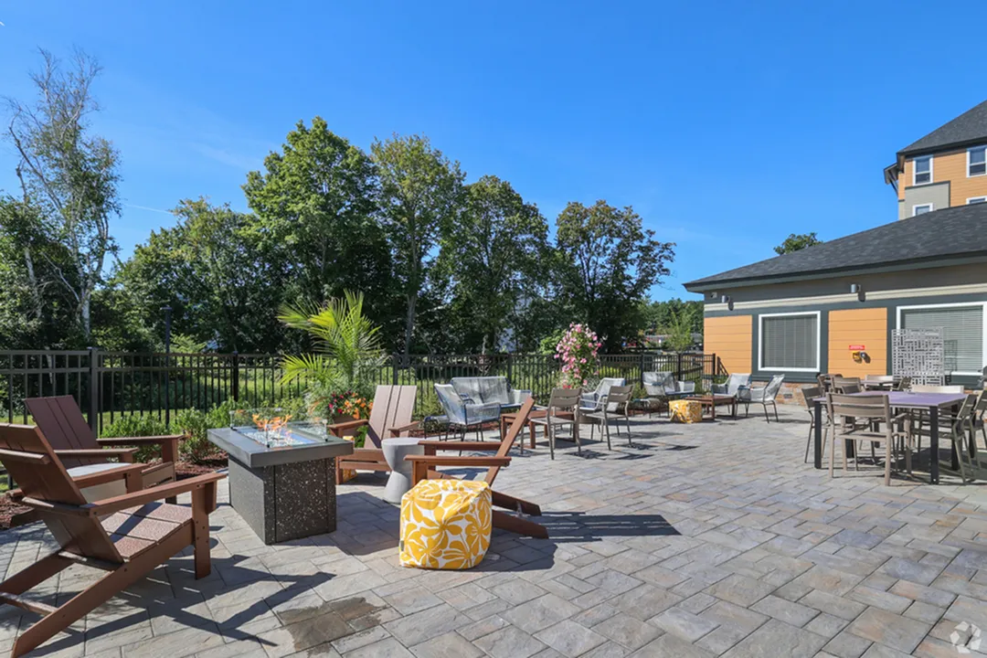 Vibrant outdoor patio with stylish seating, modern fire pit, and lush greenery, perfect for relaxing under clear blue skies.