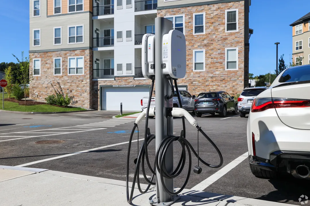 Modern apartment building with EV charging station in a well-maintained parking lot, showcasing sustainable living amenities.