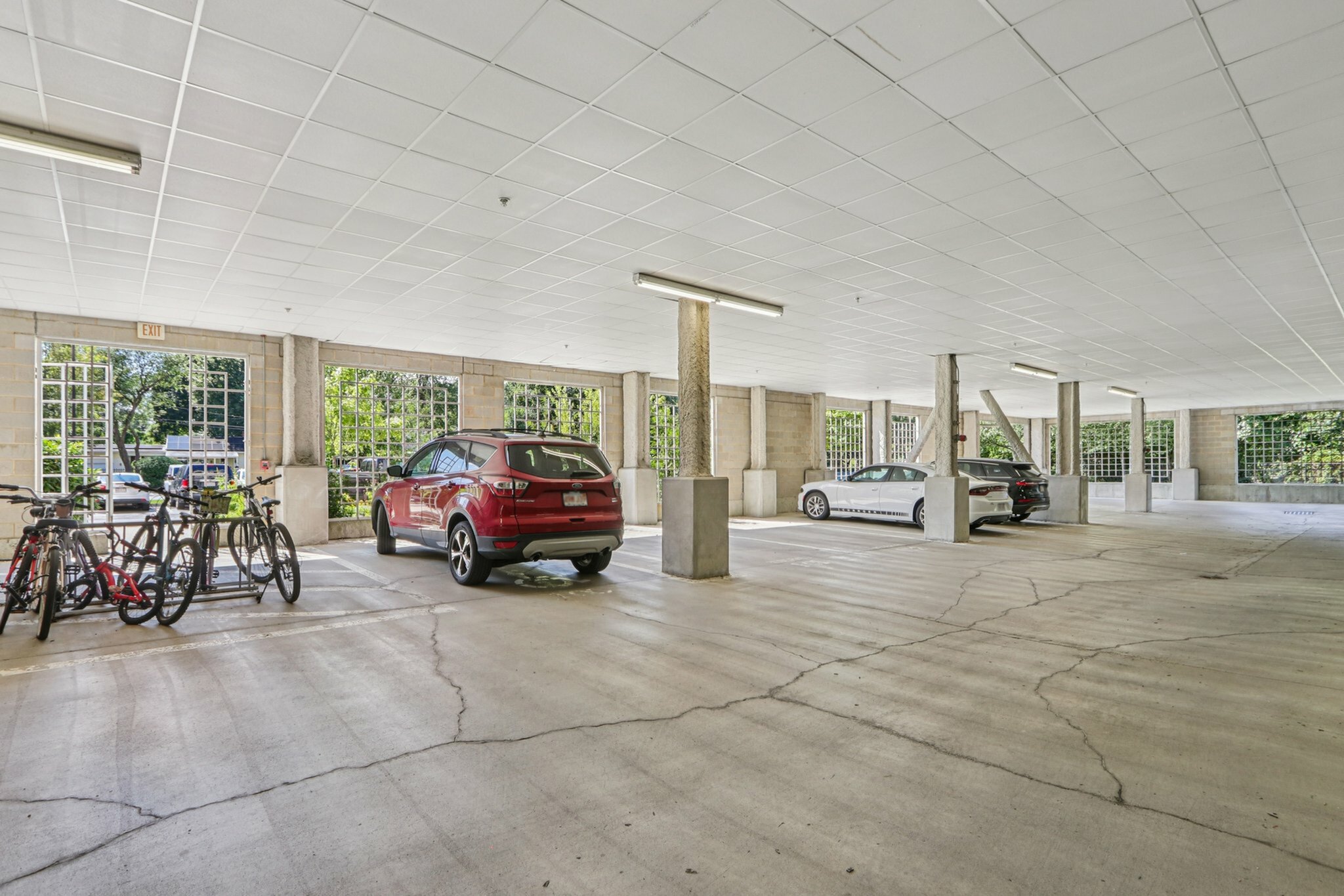 Inviting covered parking garage featuring spacious areas for cars and bicycles, enhanced by natural light through large windows.